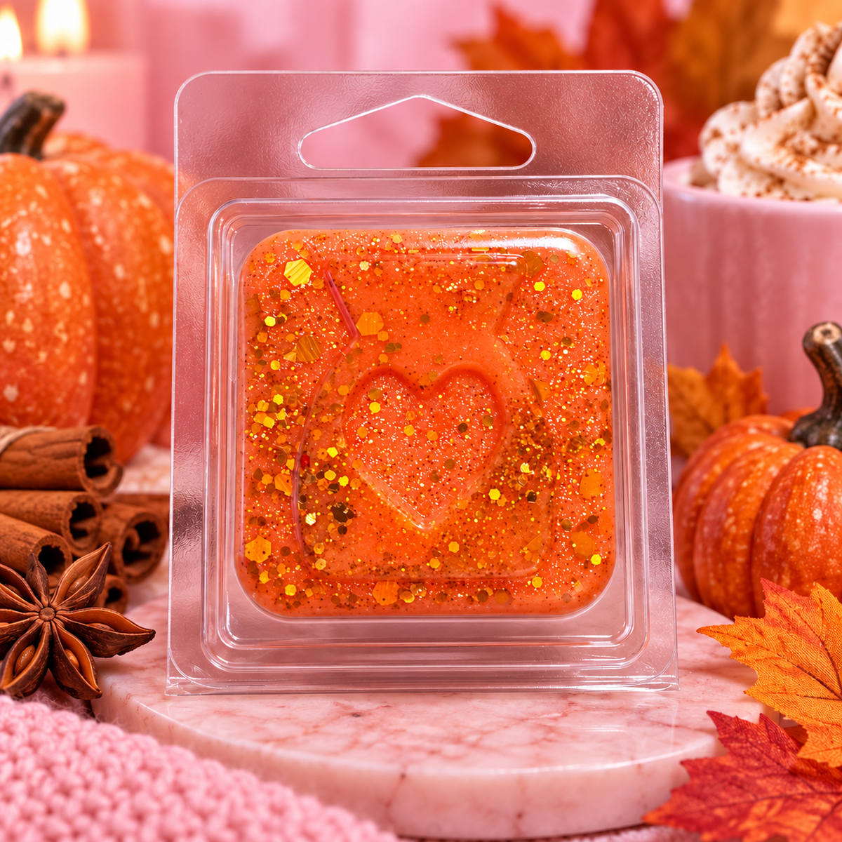 Orange Pumpkin Spice sample wax melt with a heart design and gold flecks beside pumpkins and spices.
